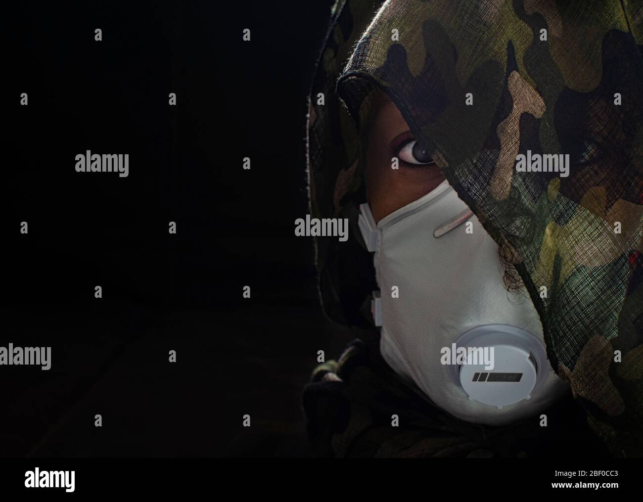 Foto concettuale di una donna guerriera che indossa una maschera FFP3 e un involucro di testa camuffato. Guerra biologica. Arma letale del coronavirus. Messa a fuoco selettiva su Foto Stock