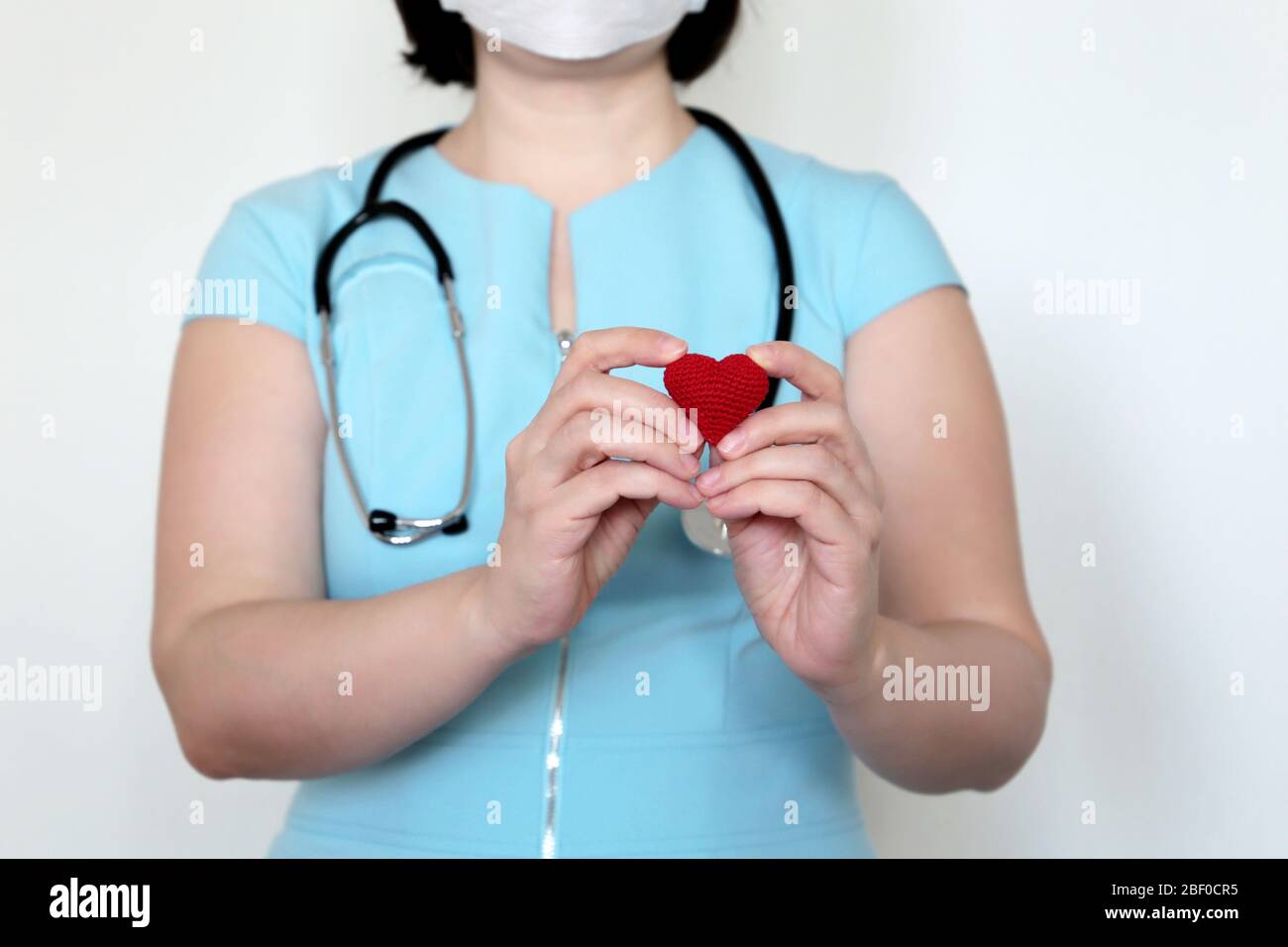 Salvare vite durante una pandemia di coronavirus 19 covid, medico della donna in maschera medica che tiene il cuore rosso lavorato a maglia nelle mani. Concetto di cardiologo Foto Stock
