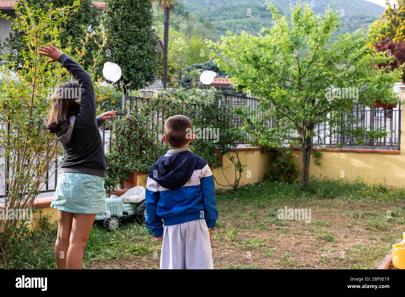 Ragazzo e ragazza togliere la maschera medica e andare a giocare in giardino, dopo la quarantena coronavirus Foto Stock