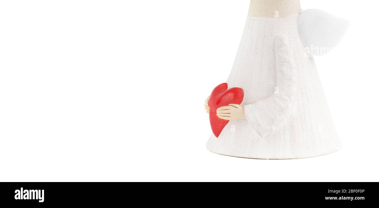Statuina d'angelo in ceramica in un lungo accappatoio bianco tiene un grande cuore rosso con entrambe le sue mani molto dettagliate. Concetto di carità di estendere l'amore e la gentilezza Foto Stock