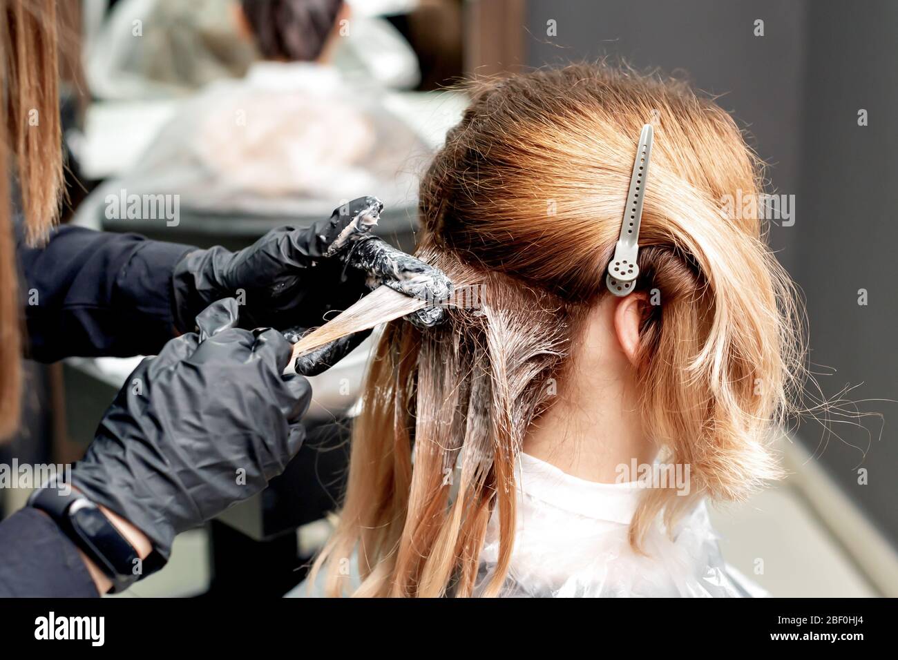 Le mani del parrucchiere tingere i capelli della donna che indossa i guanti neri nel salone dei capelli. Colorazione dei capelli. Foto Stock