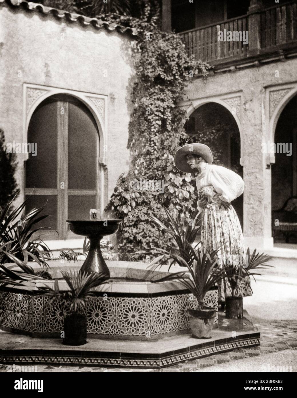 1920 DONNA ALLA MODA VESTITA GRANDE BRM HAT ABITO FULL MANICHE STAMPA GONNA GUARDANDO IN PIASTRELLE FONTANA IN STILE SPAGNOLO ATRIUM - B2075 HAR001 HARS STILE DI VITA STORIA ARCHITETTURA FEMMINE HOME VITA COPIA SPAZIO MEZZA LUNGHEZZA SIGNORE PERSONE PIASTRELLE B & W STRUTTURA AVVENTURA BALCONE STILI DI SVAGO ESTERNO ESCAPE MANICHE ELEGANTI PIASTRELLE ATRIUM MODE METÀ-ADULTO DONNA MEDIO-ADULTA ARCHI NERO E BIANCO BRM ETNIA CAUCASICA CORALLO GABLES HAR001 VECCHIO STILE Foto Stock