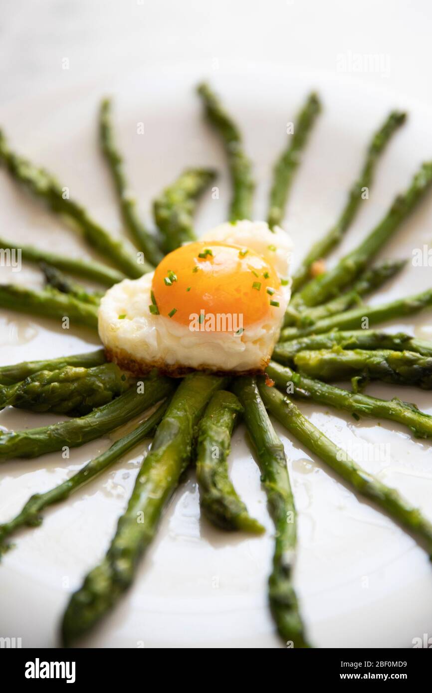 primo piano verticale di un piatto con asparagi freschi e un uovo fritto a forma di cuore su un piatto bianco Foto Stock