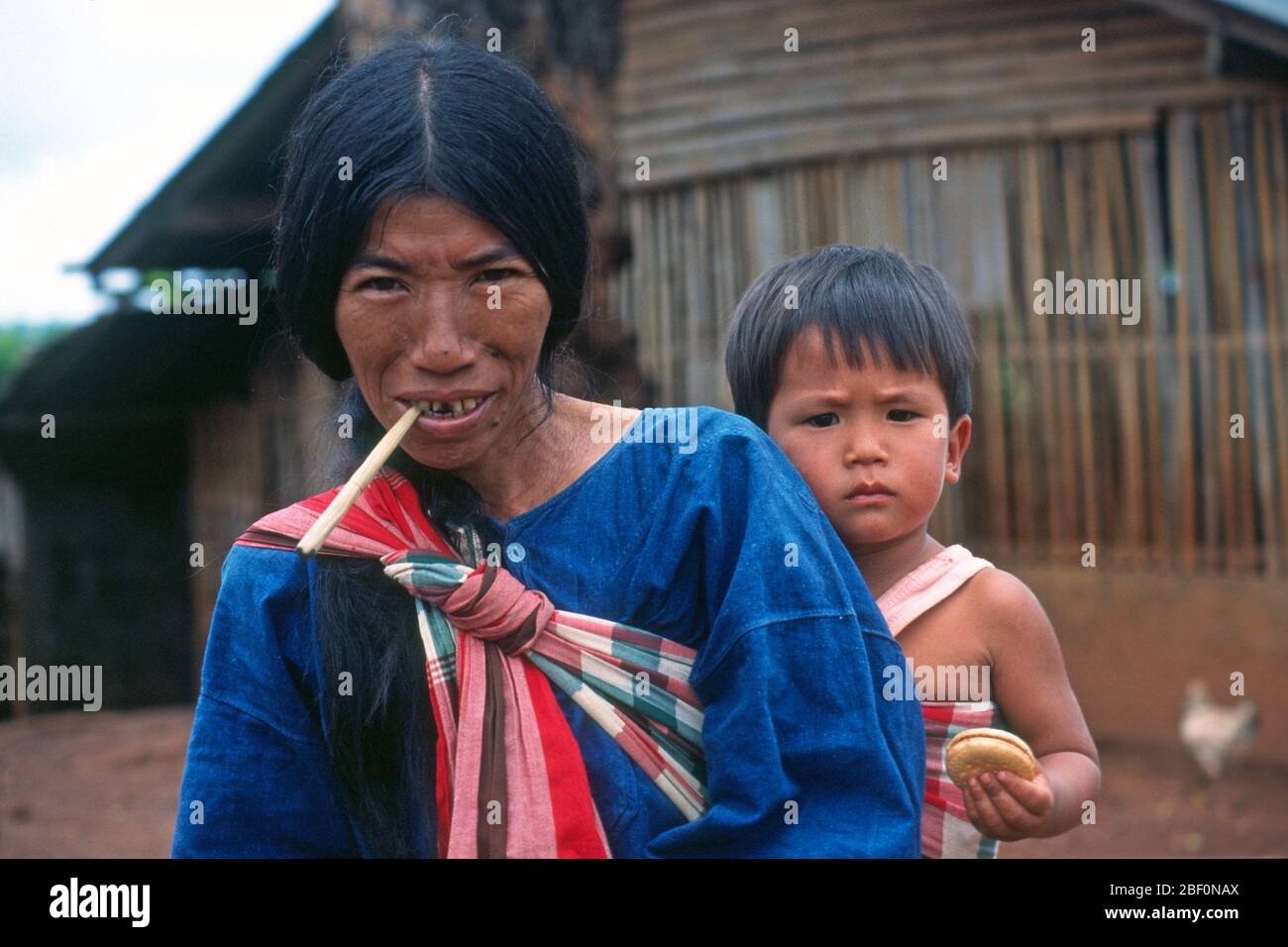 La tribù di Lahu collina donna in un villaggio nel nord della Thailandia porta il suo bambino sulla sua schiena in un colorato, fionda a motivi geometrici. Foto Stock