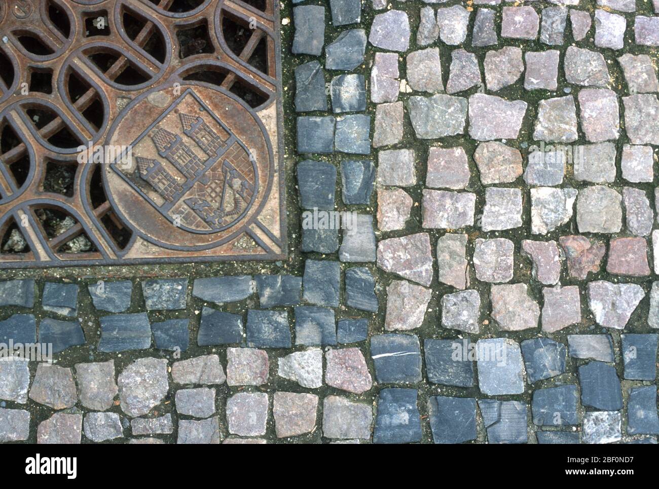 Dettaglio di una strada acciottolata e di una coperta di drenaggio ornata con il stemma della Città di Praga, Repubblica Ceca. Il centro storico di Praga è patrimonio dell'umanità dell'UNESCO. Foto Stock