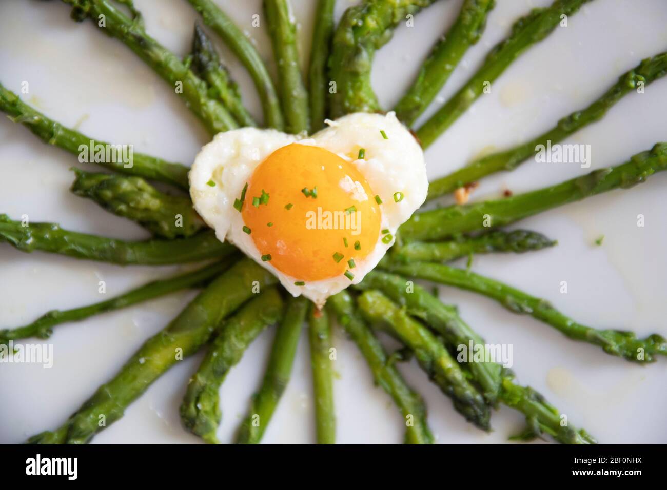 vista dall'alto orizzontale primo piano di un piatto con asparagi e un uovo a forma di cuore con alcune erba cipollina Foto Stock