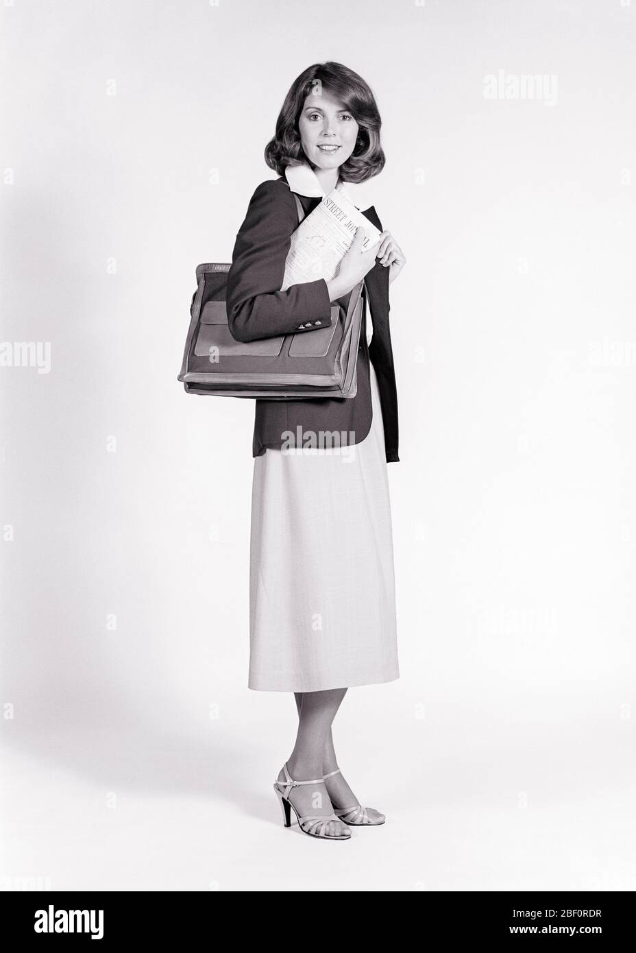 1970 1980 RITRATTO DONNA CHE GUARDA LA FOTOCAMERA INDOSSARE GONNA MIDI BLAZER BLUSA SCURO SOPRA LA SPALLA BORSA PORTADOCUMENTI - S21543 HAR001 HARS GESTIONE BLAZER FIDUCIA DIRIGENTI B&W BUSINESSWOMAN OCCHIO CONTATTO OCCUPAZIONE VENDERE FELICITÀ STILI CARRIERE LEADERSHIP BLUSA OCCUPAZIONI BOSS VENDITORE SALESWOMEN ELEGANTE BUSINESSWOMMEN MEZZO SORRISO VETRO SOFFITTO MODE MANAGER DONNA MID-ADULTA MID-ADULTA MIDI BIANCO E NERO ETNIA CAUCASICA HAR001 TACCHI ALTI VECCHIO STILE Foto Stock