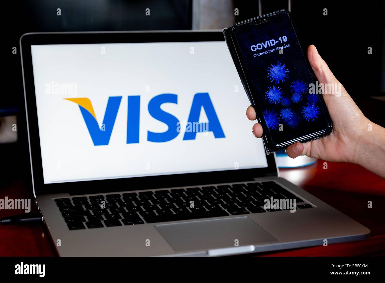 Ostrowiec, Polonia - 14 aprile 2020: Una donna detiene l'illustrazione di Coronavirus nel suo telefono cellulare di fronte a uno schermo di computer con il logo VISA per l'illust Foto Stock