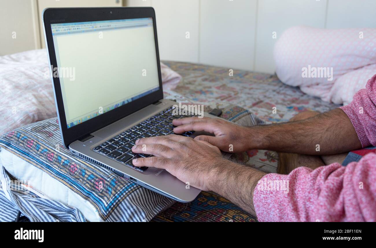 Luogo di lavoro di fortuna dove un maschio adulto sta lavorando dalla sua camera da letto con cuscino per sostenere il suo laptop durante la pandemia del covid-19, Svezia Foto Stock