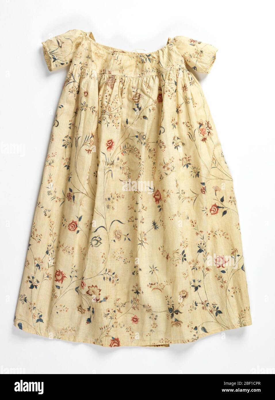 Abito per bambini. Abito per bambini con un motivo di delicati spray floreali nei colori blu, rosso, lavanda e marrone su bianco. La gonna è raccolta in un giogo, che ha una scollatura con filo di trazione, con maniche corte; aprire il retro. Foto Stock