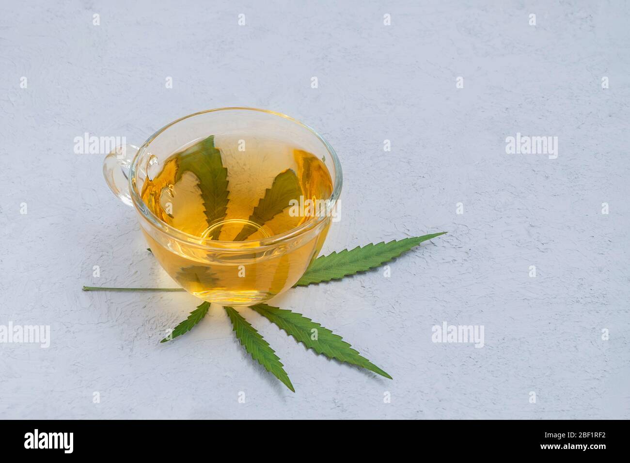 Tè di cannabis in una tazza di vetro con foglie di marijuana su fondo neutro di cemento con spazio per le copie Foto Stock