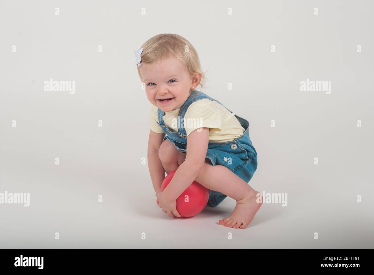 Adorabile bambina di 18 mesi sorridente mentre tiene una palla rosa nello studio fotografico della sua mamma a Playa del Rey, California. Foto Stock