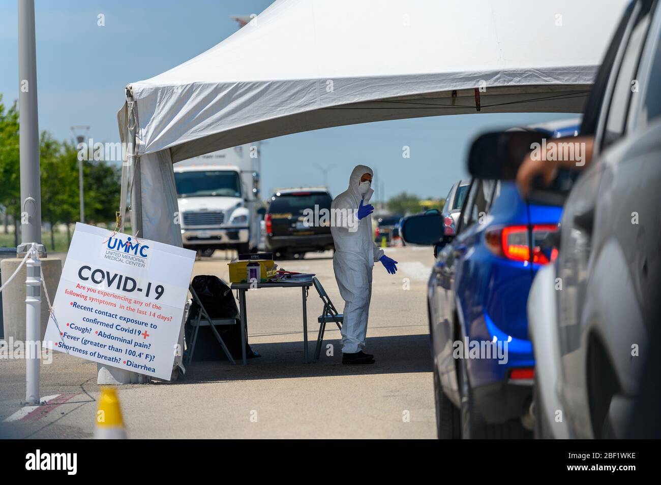 Sugar Land, Texas - 16 aprile 2020: Vestito con completo equipaggiamento protettivo un operatore sanitario raccoglie informazioni da persone sedute all'interno della loro auto a t Foto Stock