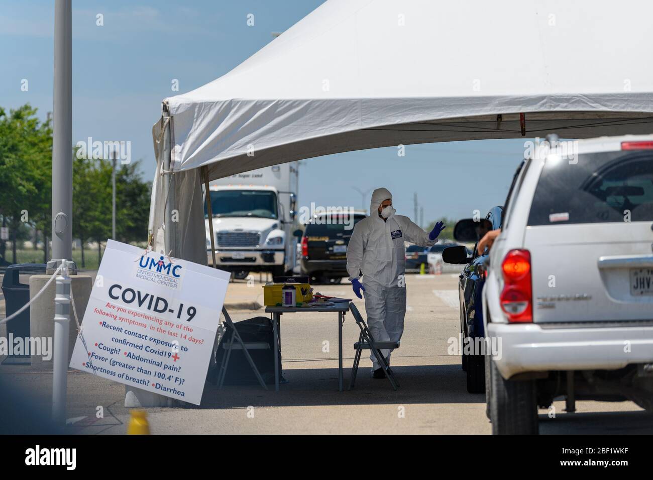 Sugar Land, Texas - 16 aprile 2020: Vestito con completo equipaggiamento protettivo un operatore sanitario raccoglie informazioni da persone sedute all'interno della loro auto a t Foto Stock