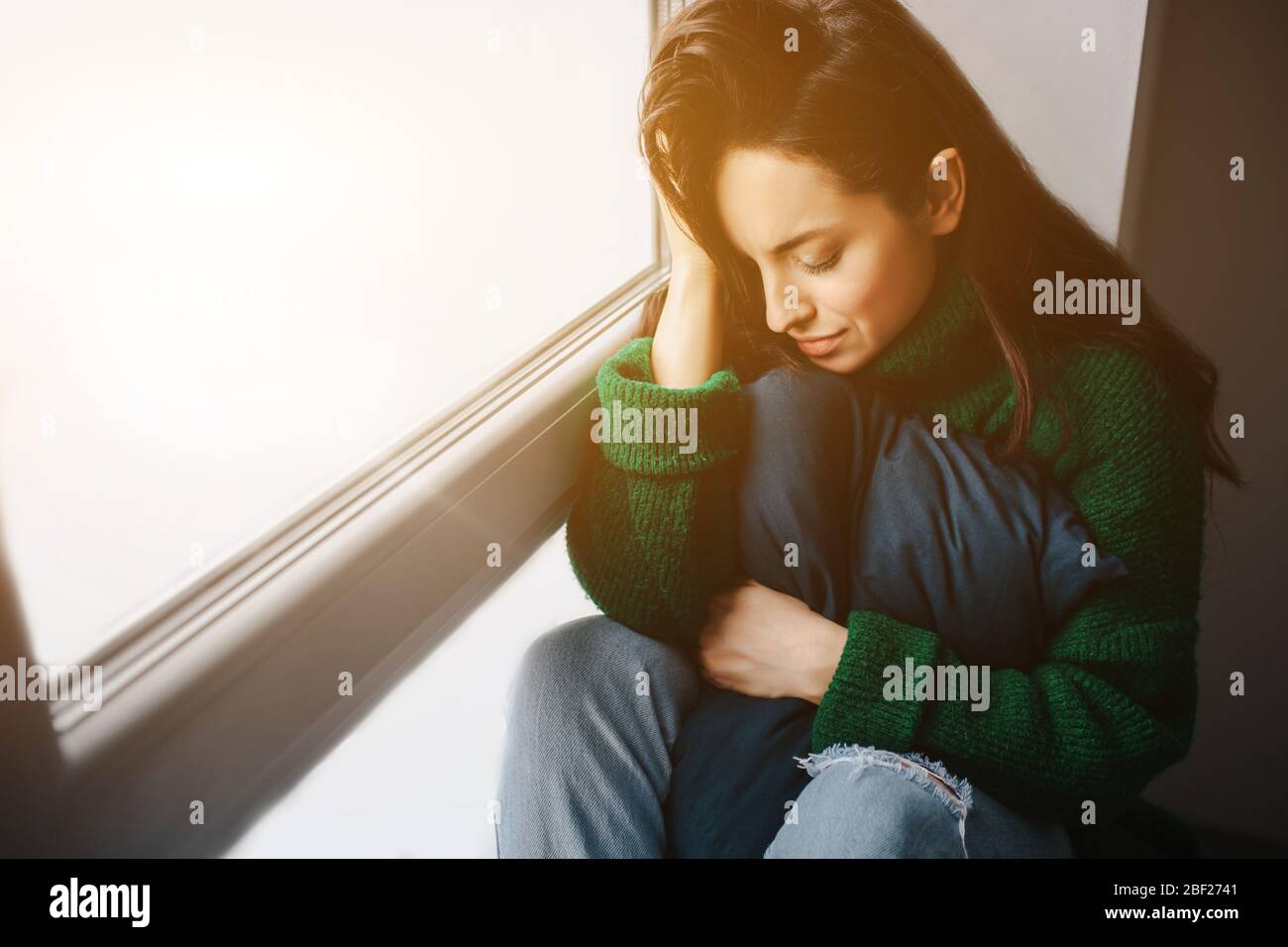giovane donna infelice è triste vicino alla finestra. La brunetta piange. Tristezza, apatia, depressione e melancolia. Foto Stock