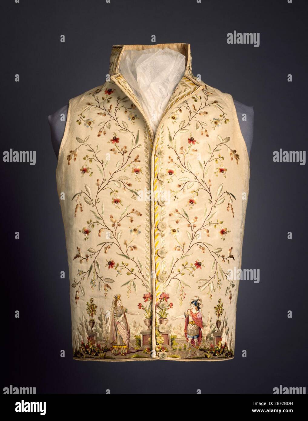 Gilet. Gilet in seta bianca con colletto alto e bordo diritto. Bordo molto profondo ai bordi anteriori di una vite curvata e fiorita. In fondo, figure ricamate in abito classico si trovano davanti ad una balaustra di pietra con urne di fiori e alberi da frutto. Foto Stock