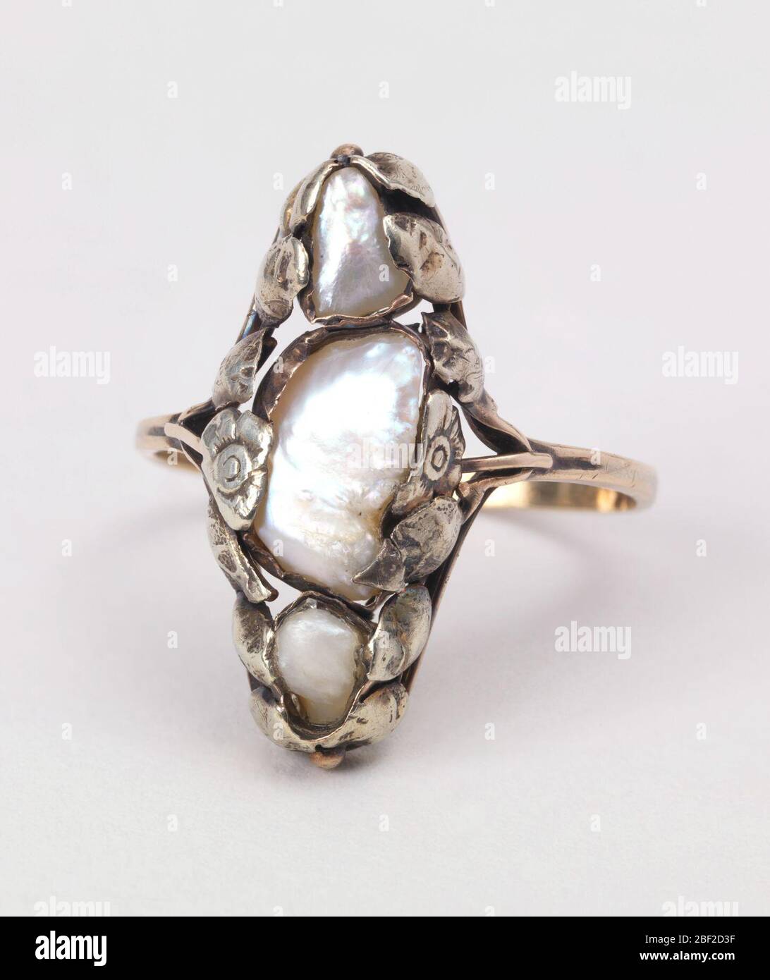 Anello del dito. Tre perle d'acqua dolce irregolari allineate verticalmente e incorniciate all'interno di un bordo di fiori d'oro e foglie, montate su una sottile fascia d'oro. Foto Stock