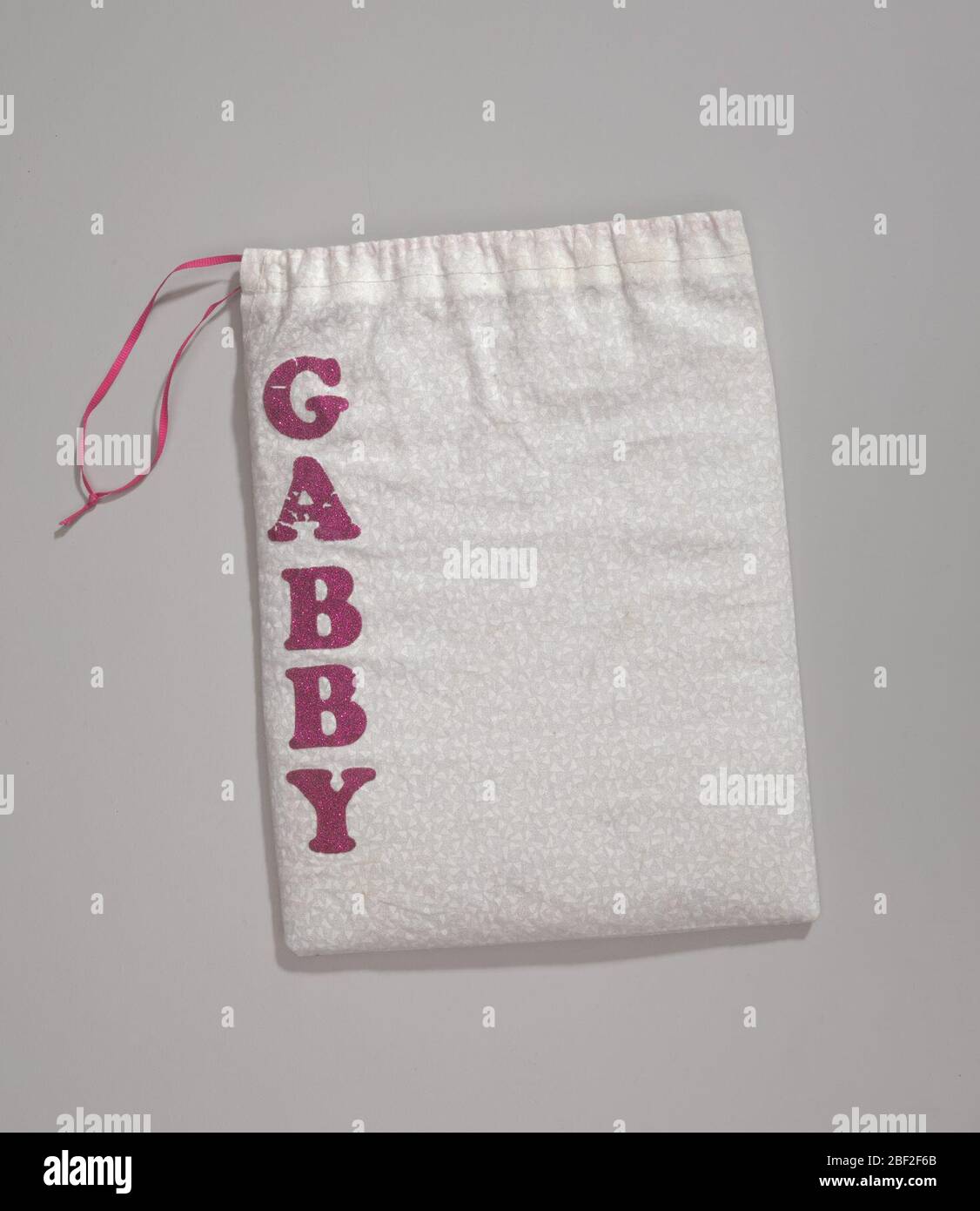 Borsa utilizzata da Gabby Douglas per trasportare le impugnature e il nastro non uniformi per le Olimpiadi del 2012. Borsa con coulisse bianca. Sul tessuto è presente un leggero motivo grigio. C'è una corda rosa in cima al lato destro del sacchetto. Il nome [GABBY] sta scendendo sul lato destro della borsa con lettere rosa scuro scintillanti. Foto Stock