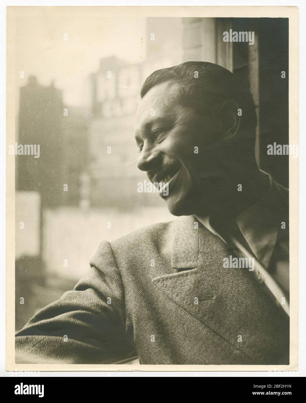 Stampa di Cab Calloway che guarda fuori una finestra. Una fotografia in bianco e nero di Cab Calloway che guarda fuori una finestra della città. Calloway è raffigurato dal petto in su, le sue spalle appoggiate su una cornice della finestra, il suo braccio destro proprio teso lungo la soglia. Foto Stock