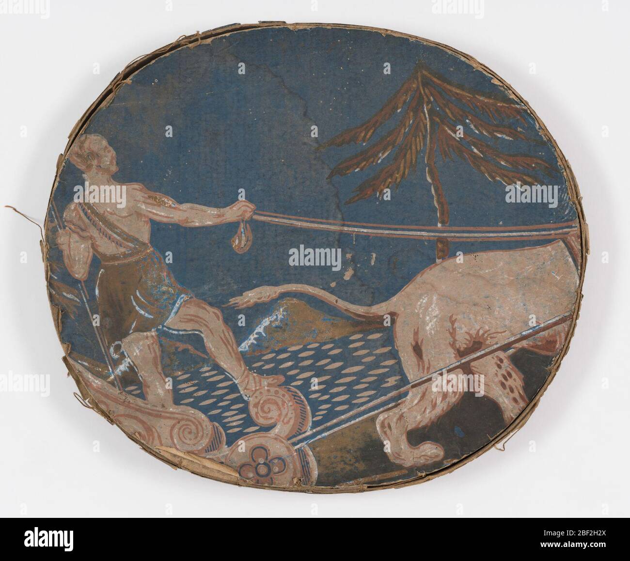 Bandbox. Coperchio del bendbox per il pateboard coperto da carta da parati: Sfondo blu, figura maschile in piedi in carro trainato da leone (solo parte posteriore del leone visibile) in castoni, marrone. Bordo: Terra blu nera, tre linee di piccoli punti blu, una linea di grandi punti bianchi e rosa. Foto Stock