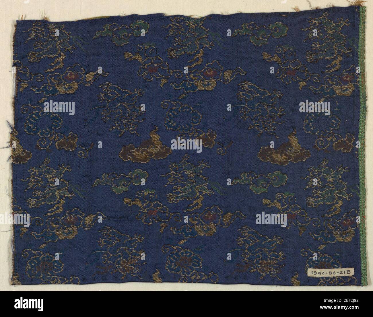Frammento. Disegno di draghi, forme floreali e nuvole volanti in trame supplementari di oro, verde, rosso, azzurro seta e fili d'oro su terra blu scuro twill. Foto Stock