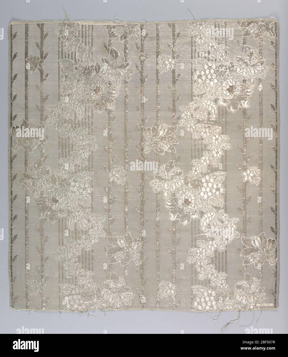 Tessile. Tessuto a righe bianco e argento con trama supplementare di strisce piatte d'argento i cui galleggianti formano strisce verticali con foglie a intervalli. Galleggianti bianchi della trama forma contorni per serpentina spray floreali sparsi sulle aree a strisce. Foto Stock