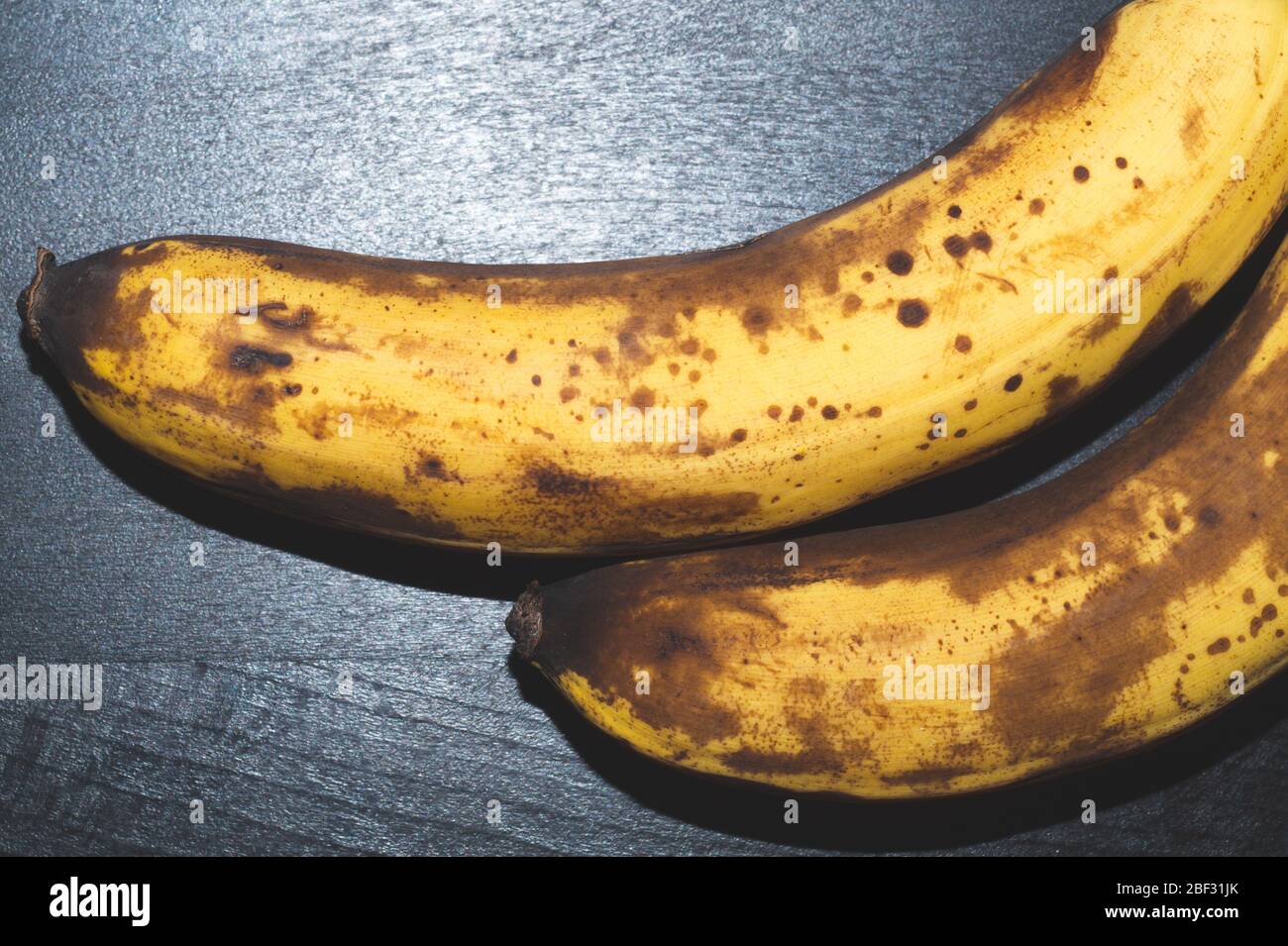 Banane overmature con macchie. Frutta si deposita su tavolo di legno nero Foto Stock