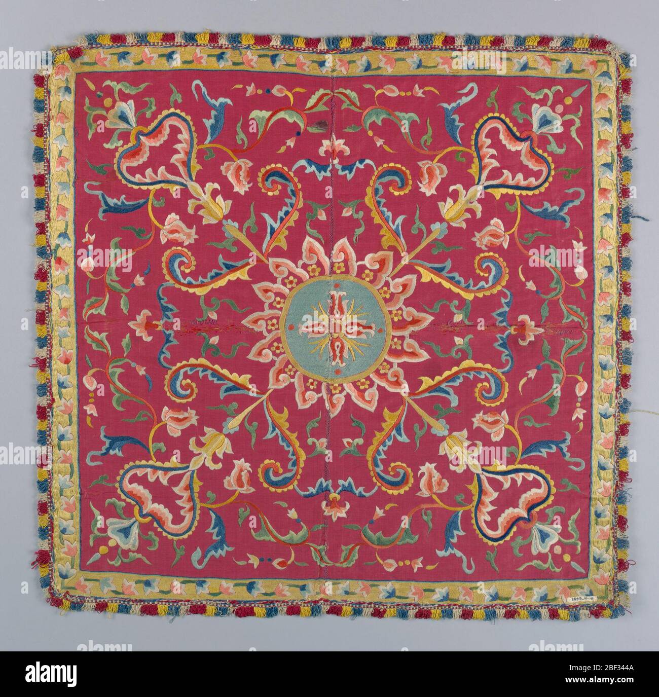 Tappetino da tavolo. Pannello quadrato di seta rossa a coste orizzontali con ricamo in seta multicolore. Medaglione centrale circolare floreale, circondato da fiamme. Dal medaglione, rami diagonali, molto convenzionati, con fiori e foglie, corrono ad ogni angolo del pannello. Foto Stock