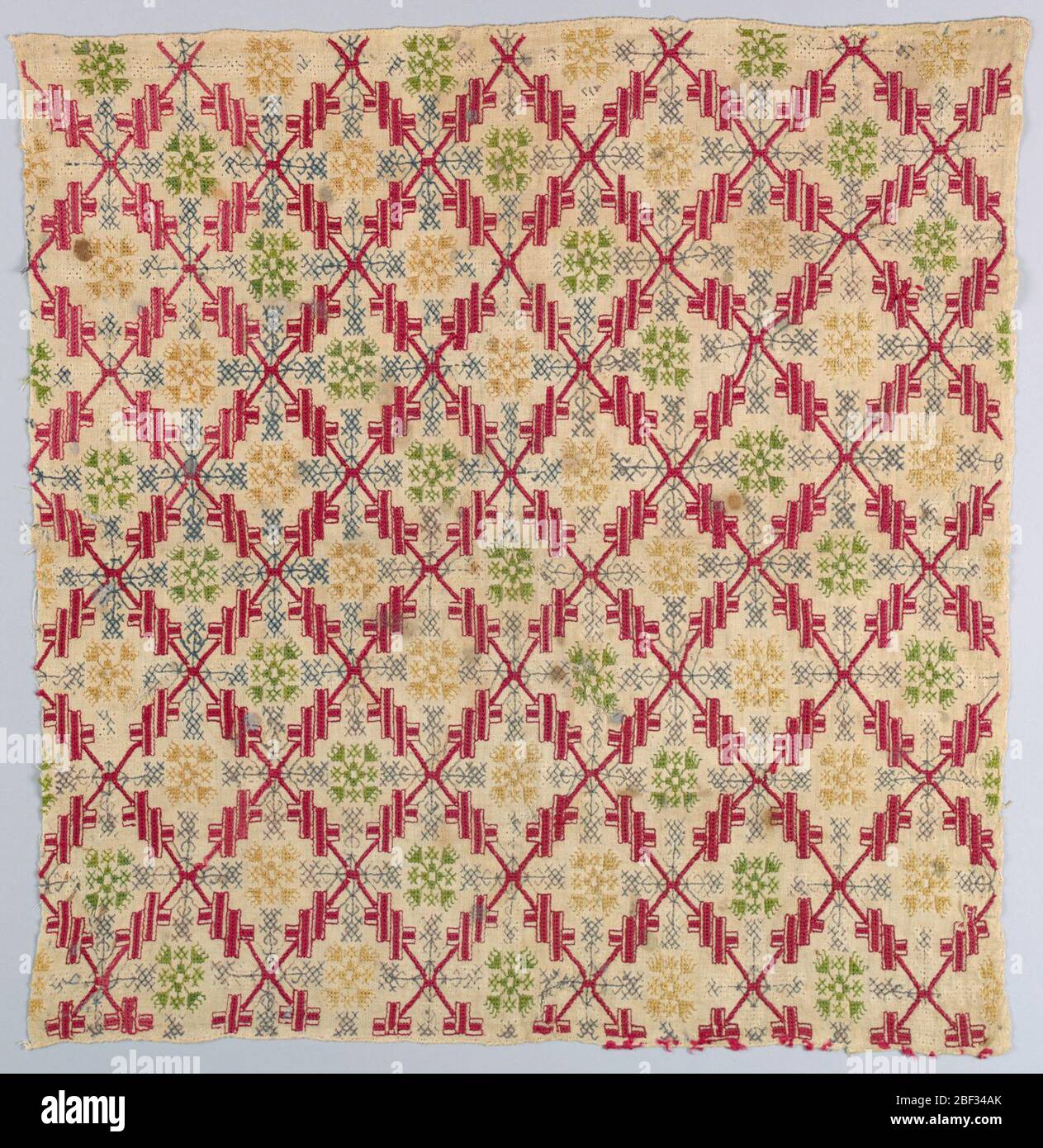 Copertura. Copertura quadrata in reticolo a diamante che racchiude fiori geometrici in seta rossa, verde, blu e gialla su un terreno di lino. Foto Stock