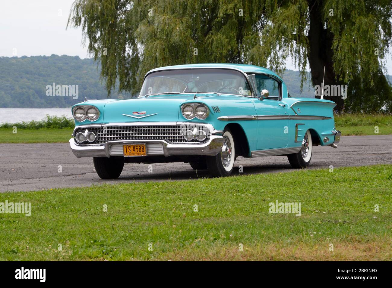 Turquoise 1958 Chevrolet Impala coupé tre quarti di vista frontale contro salice albero al lago Foto Stock