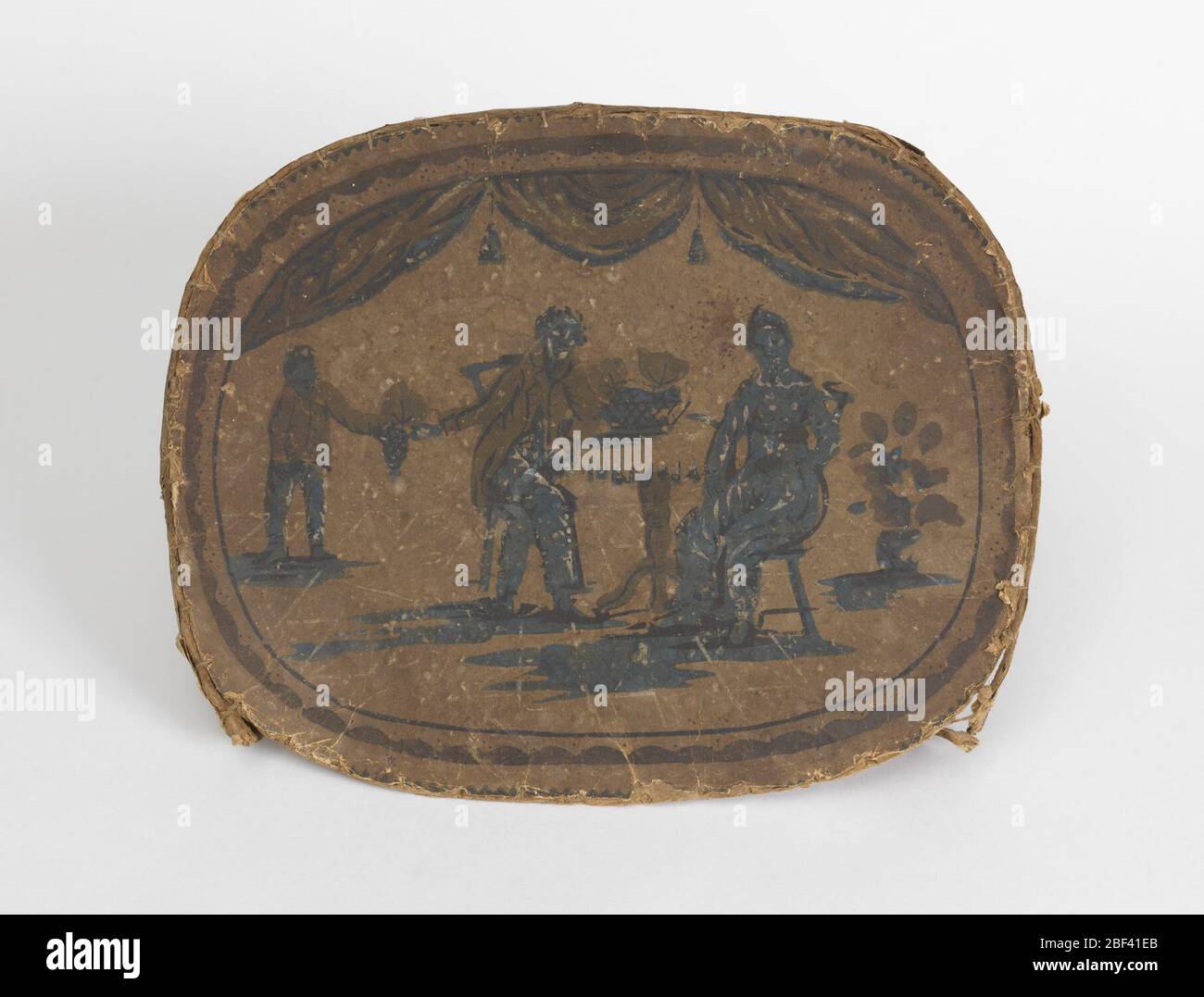 Bandbox. Solo coperchio. Su quello che può essere stato sfondo bianco, scena incorniciata in una cornice ovale di linee blu: Uomo e donna seduti in sedie a tavolino con cesto di uva, ragazzo in piedi vicino mani uva all'uomo. Blu, marrone, giallo sbiadito o verde. Foto Stock