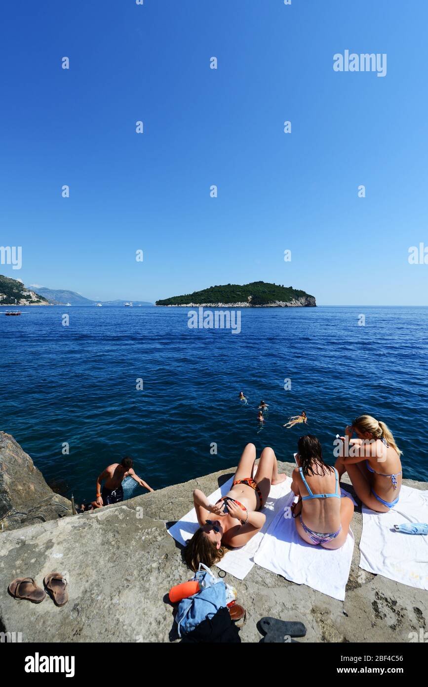 Il turista si immergono nel sole sulle scogliere vicino alle mura della città vecchia di Dubrovnik sulla costa adriatica in Croazia. Foto Stock