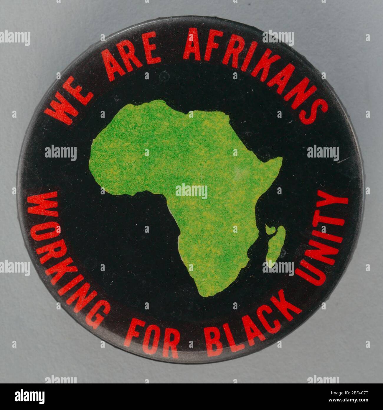 Pulsante Pinback che promuove l'unità nera. Pulsante rotondo con pin-back che mostra l'immagine verde centrale del continente africano. Il tipo rosso circoli l'Africa e legge [SIAMO AFRIKANS/LAVORANDO PER L'UNITÀ NERA]. Foto Stock