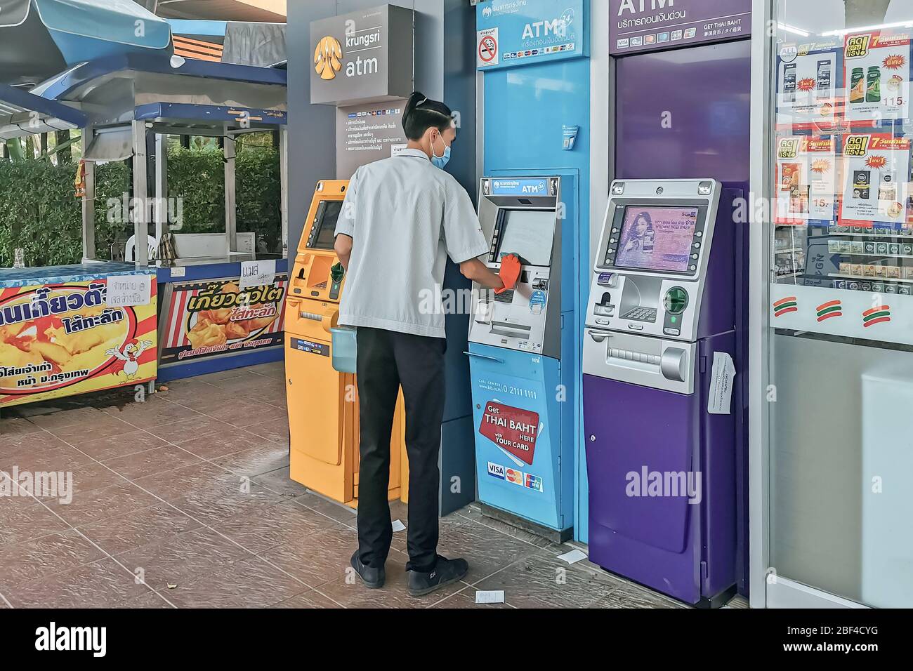KANCHANABURI, THAILANDIA - 12 APRILE 2020 : ufficiale maschile non identificato pulire ATM con alcool a misure preventive contro il virus corona (Covid-19) in Foto Stock