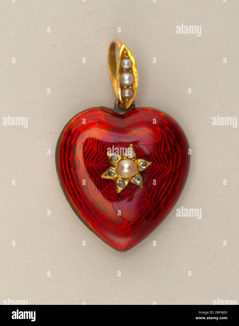 Locket nella forma di un cuore. A forma di cuore, rosso smaltato, con perla e piccoli diamanti al centro; sul retro un vano circolare per il cesto; anello e anello con tre punte perlate. Foto Stock