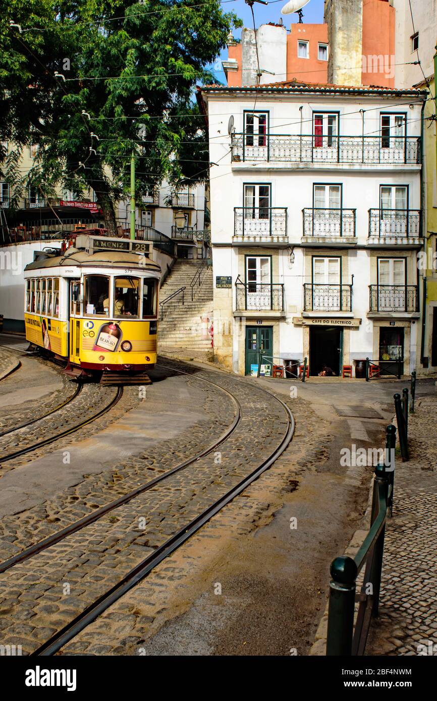 Il tram elettrico giallo 28 scende su una collina passando davanti a una casa bianca con balconi nel quartiere di Alfama a Lisbona Foto Stock