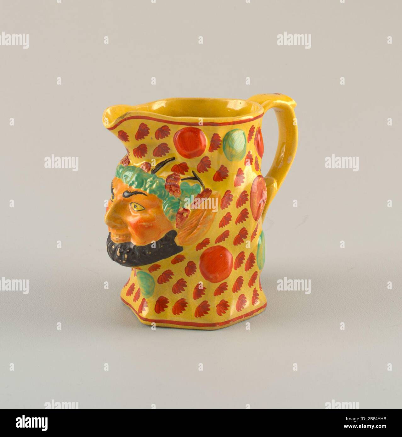 Caraffa. Maschera Satyr con barba nera con orecchie appuntite e capelli verdi proietta fuori dalla caraffa. Il resto della caraffa è decorato con foglie rosse e cerchi su terreno giallo. Aprire il beccuccio; bordo rosso intorno al bordo e alla base. Foto Stock