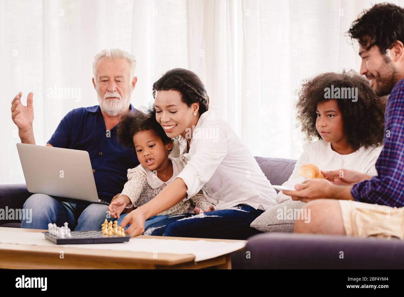 Bella casa felice famiglia che vivono insieme in soggiorno padre madre e nonno giocare con figlia mix gara. Foto Stock