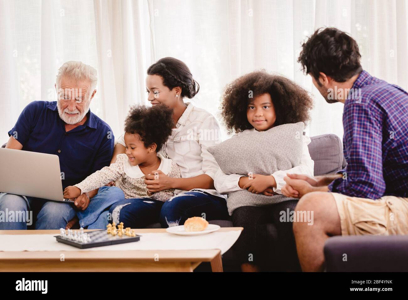 Bella casa felice famiglia che vivono insieme in soggiorno padre madre e nonno giocare con figlia mix gara. Foto Stock