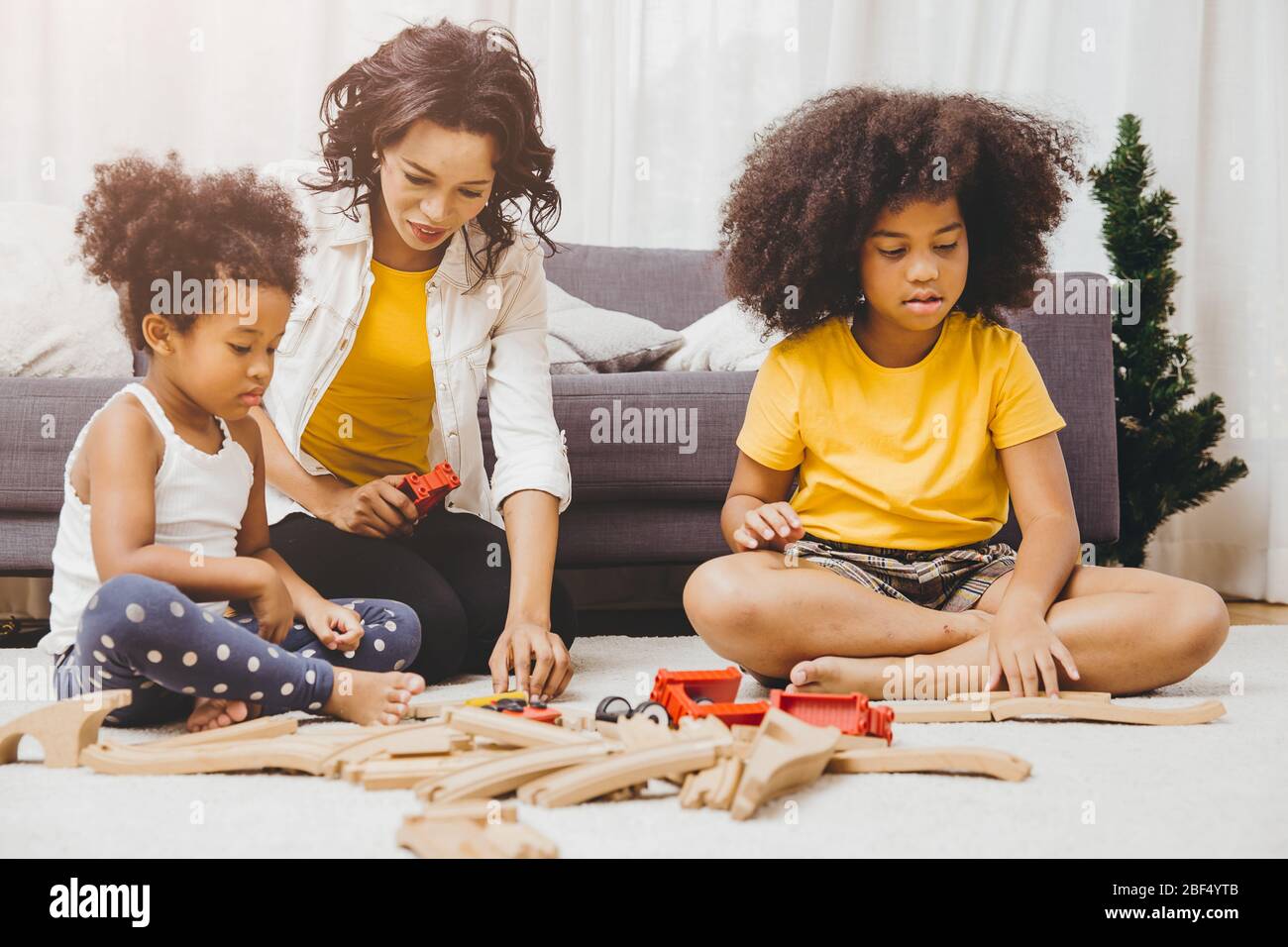 Single mamma che vive con due figlia imparare e giocare puzzle giocattolo in casa appartamento. Nanny che guarda o bambini a persone nere soggiorno. Foto Stock