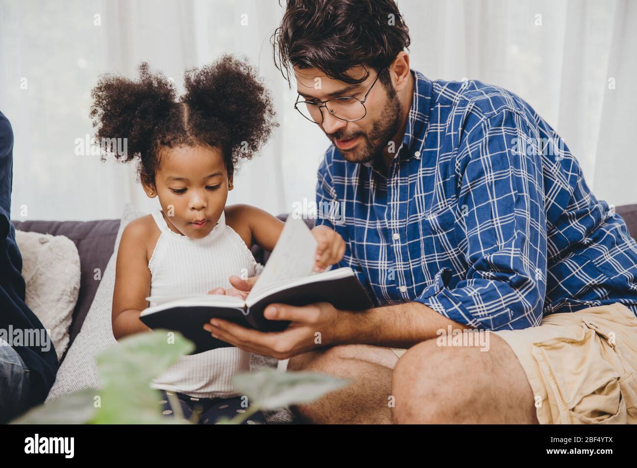 Piccolo bambino carino che osserva l'amore stupire a leggere il libro ed imparare il supporto dal padre al concetto intelligente del capretto. Foto Stock