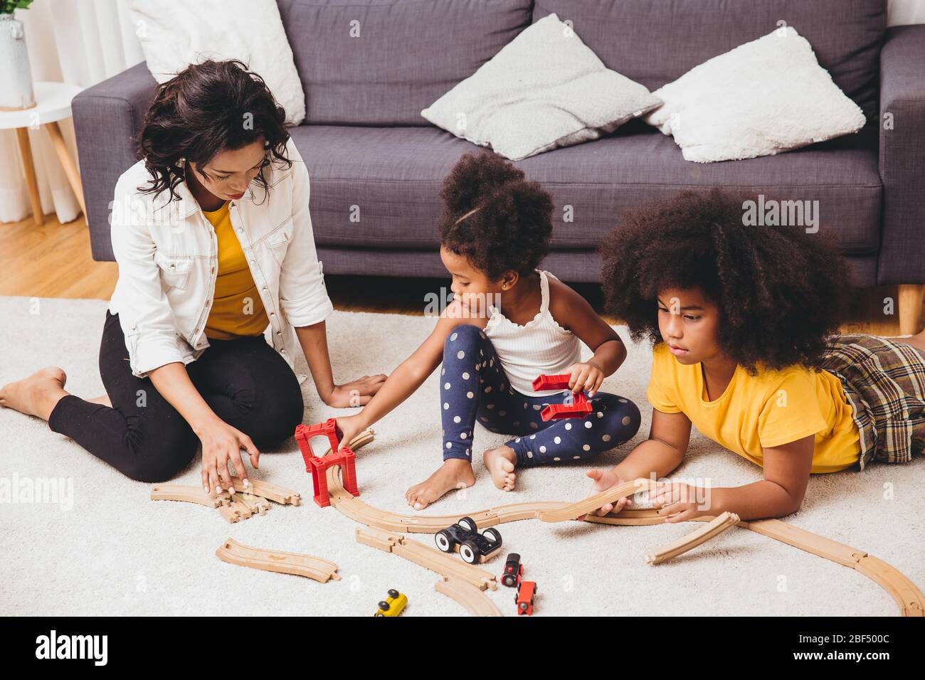 Madre genitore che gioca con i bambini che imparano a risolvere il puzzle giocattolo a casa appartamento. Nanny che guarda o bambini a persone nere soggiorno. Foto Stock