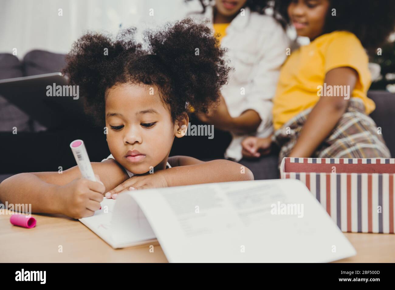 Bambina piccola ragazza pelle nera facendo i compiti a casa con la sorella e la madre. Foto Stock