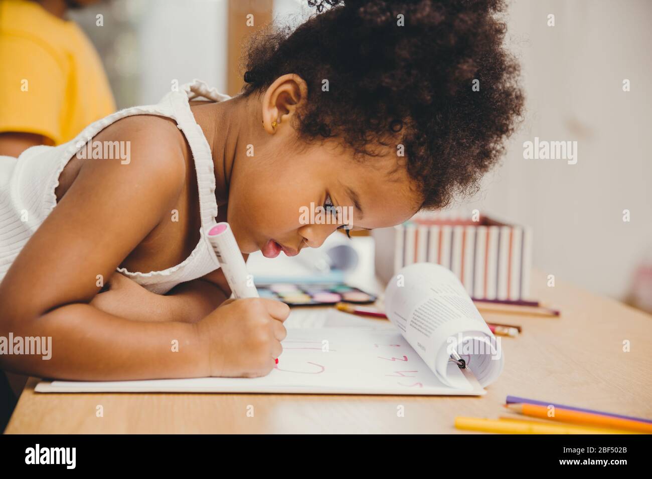 Closeup piccola ragazza di pelle nera scrittura facendo i compiti a casa. Foto Stock