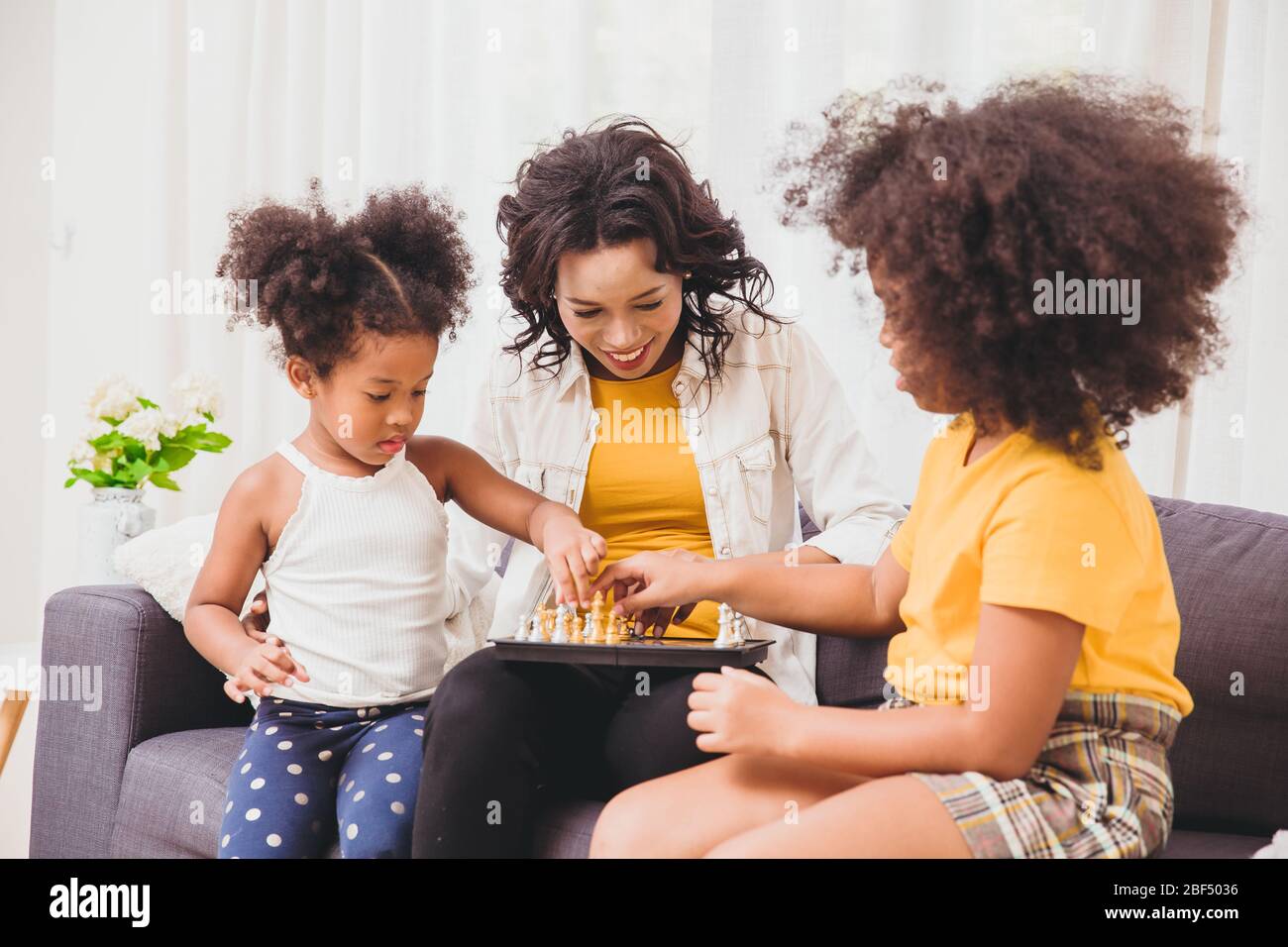 Madre intelligente buona cura, insegnando ai suoi bambini di essere genio e ragazze intelligenti che imparano a giocare a scacchi gioco di ruolo in vacanza a casa. Foto Stock