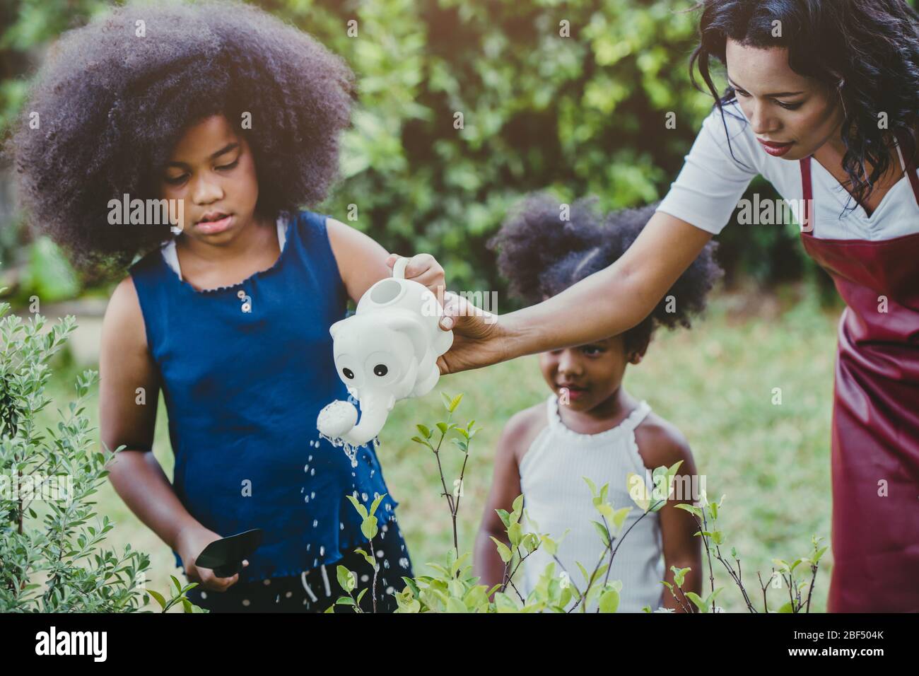 Famiglia bella giardinaggio annaffiatura verde attività vegetale con i bambini durante il soggiorno a casa per ridurre lo scoppio del Coronavirus. Bambini che annaffia t Foto Stock