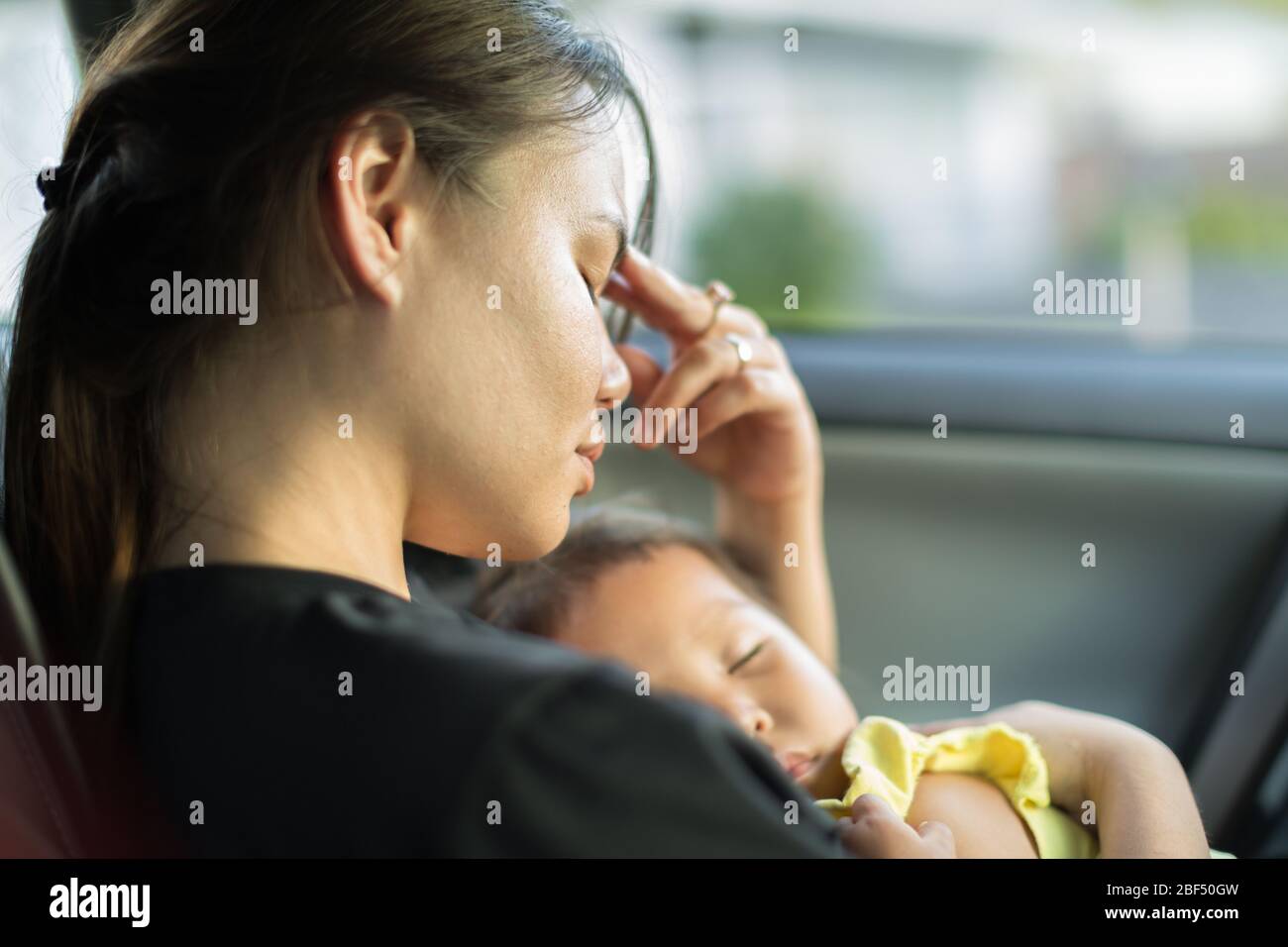 Una mamma infelice esaurita cercando di prendere un pisolino con il suo bambino in auto. Foto Stock