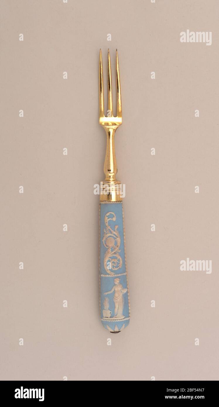 Forcella. Forcella dorata in argento con tre denti curvi, collo a forma di balaustra, sezione ovale. Boccola con bandella. Manico jasper rastremato, ovale nella sezione, terra blu chiaro con disegno rialzato in bianco. A forma di S, foglie di acanto e fiori su entrambi i lati. Foto Stock