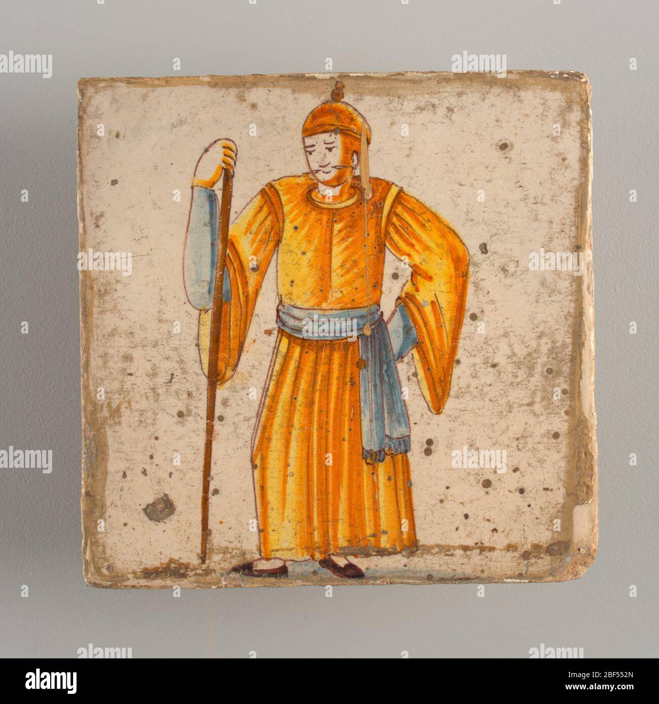 Affiancamento. Uomo in piedi, vestito con lungo costume giallo e blu sotto maniche e cintura; appoggiato sul lungo bastone che tiene nella sua mano destra. Chinoiserie tipo di decorazione. Foto Stock