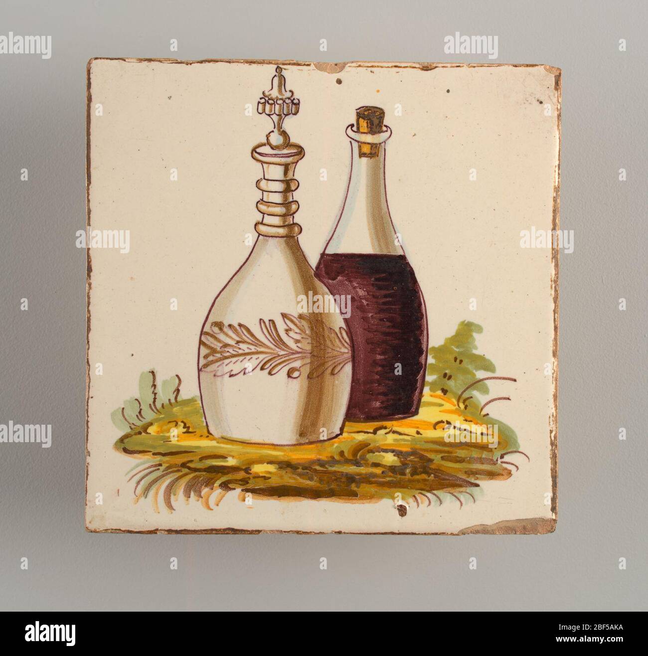 Affiancamento. Una caraffa di vetro con vino viola e una bottiglia di faience con tappo e decorazione fantasia wreath posto su un po 'di verde indistinto. Foto Stock